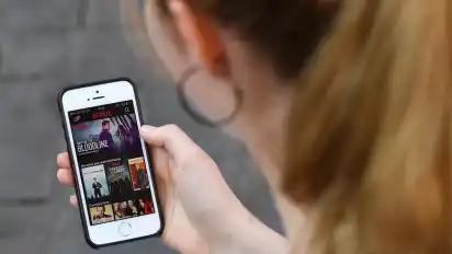 Eine junge Frau hat auf ihrem Smartphone die App vom Streaming-Anbieter Netflix geöffnet. Verbraucher können auf ihre Online-Abos für Musik, Filme oder Sport künftig auch im Urlaub zugreifen.
