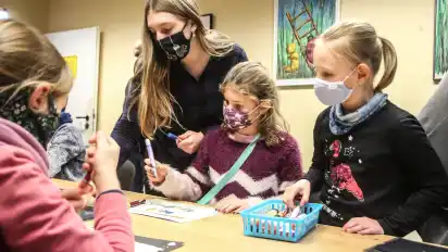In der Gruppe gestalten Mädchen im Hort ihren Mundschutz. Anschließend werden die Farben fixiert und die Maske wird von Pädagogin Angelika Wehrhahn genäht.