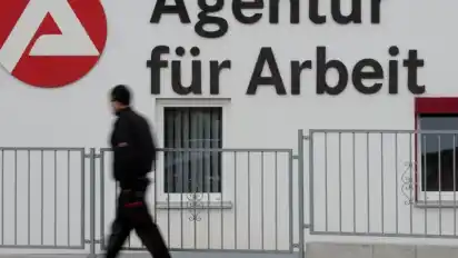 Ein Mann geht an dem Logo der Agentur für Arbeit vorbei. Foto: Sebastian Kahnert/dpa-Zentralbild/dpa