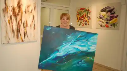 Eva-Maria Löhmann stellt ab heute in der Begegnungsstätte Schwanewede aus. In ihren Händen hält die Künstlerin das Werk „Wasserwelten“, eines ihres Lieblingsbilder. Die Gemüse-Stillleben im Hintergrund sind ihre neuesten Arbeiten. GKE·