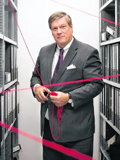 Ulrich Emde im Archivraum seiner Kanzlei im Technologiepark Universtität. Mit einer Schere schneidet er symbolisch den roten Faden ab. Die Serie geht mit ihm zu Ende.