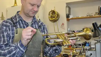 Blechblasinstrumentebaumeister Daniel Kunst lötet das Mundrohr einer Trompete.