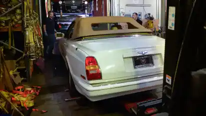 Zwei Mitarbeiter achten darauf, dass das Auto per Gabelstapler vorsichtig aus dem Rack-System im Container gezogen wird. Danach müssen sie noch einen Ford Mustang aus seiner Befestigung befreien und herausziehen.