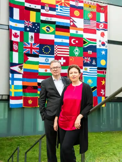Kunsthallenchef Christoph Grunenberg und Modeschöpferin Sibilla Pavenstedt vor dem Flaggenteppich an der Fassade des Gebäudes: Ein Symbol für Vielfalt und Offenheit.