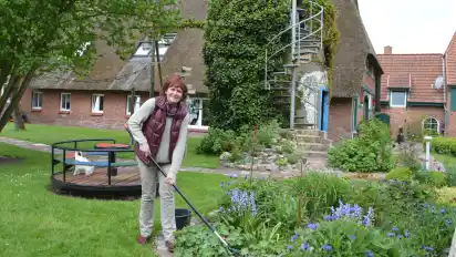 Gartenfreundin Karin Hogrefe bei der Arbeit in einer großen Pflanzinsel. Im Hintergrund ragt der Siloturm mit der Terrasse vor dem 251 Jahre alten Bauernhaus auf. GKE·