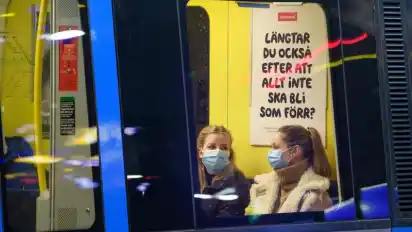 Zwei junge Frauen sitzen mit Mund-Nasen-Schutz in einer U-Bahn. Foto: Jessica Gow/TT NEWS AGENCY/AP/dpa