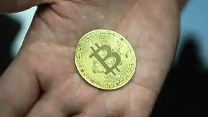 Ein Mann hält eine nachgemachte Münze mit dem Bitcoin-Logo in den Händen. Foto: Nicolas Armer/dpa