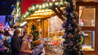 Besucher eines Weihnachtsmarktes stehen an einem Verkaufsstand für Süßigkeiten.