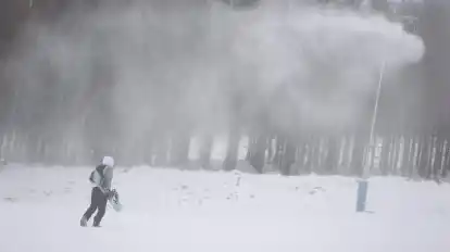 Ein Besucher geht mit seinem Snowboard an den Beschneiungsanlagen am Wurmberg Braunlage entlang.