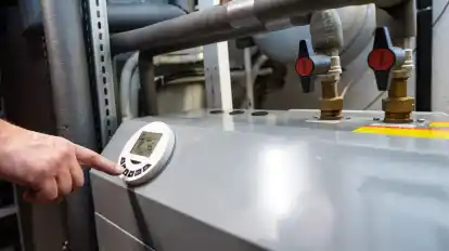 Ein Mann bedient eine Luftwärmepumpe, die im Keller eines Wohnhauses steht.
