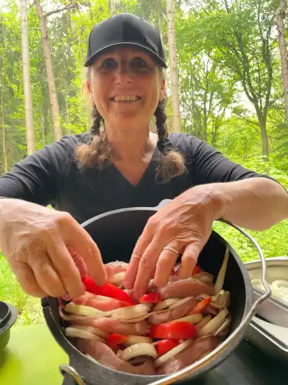 Schicht für Schicht werden Paprika, Nackensteaks, Zwiebelringe und Bacon fest gestapelt. Dafür kippt Lagerfeuerköchin und Waldpädagogin Andrea Kitzmann den gusseisernen Topf auf die Seite.