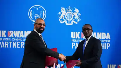 Großbritanniens Innenminister James Cleverly (l) und Vincent Birut, Außenminister von Ruanda, schütteln sich die Hände. Mit dem neuen Vertrag will die britische Regierung Asylsuchende künftig in das ostafrikanische Land abschieben.
