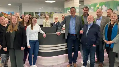 Hudes Bürgermeister Jörg Skatulla (vorne links) eröffnete mit Mitarbeitern und Gästen den neuen Standort. Innenarchitektin Bea Klauner (rechts) von der Tischlerei Sandkuhl hat die Gestaltung der Räume übernommen.