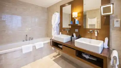 Zum großzügigen Bad in hellen Marmorfliesen gehört ein großer Waschraum mit Badewanne und zwei auf dunklem Edelholz montierten Waschplätzen.