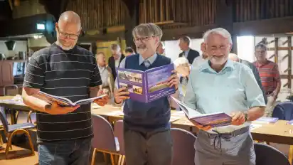 Nutzten die Gelegenheit gleich, um im neuen Buch zu stöbern (von links): Nils Meyer, Ralf Weber und Wilfried Meyer. Im Hintergrund warten die zahlreichen Mitwirkenden auf ihr Exemplar.
