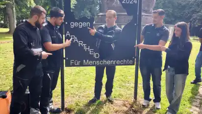 Sie haben zusammen mit ihren Azubi-Kollegen in der Lehrwerkstatt von Mercedes die Gedenktafel vom Anti-Kolonialismus-Mahnmal neben dem Elefanten restaurauriert. Abdul-Kader, Alim, Sinan, Zehra und hinten in der Mitte Ausbilder Alexander Graf zeigen. wo genau an der Tafel sie etwas gewerkelt haben. Alexander Graf hat die Buchstaben an die Tafel geschweißt und ist sich sicher: ”Das hält Jahrzehnte.”